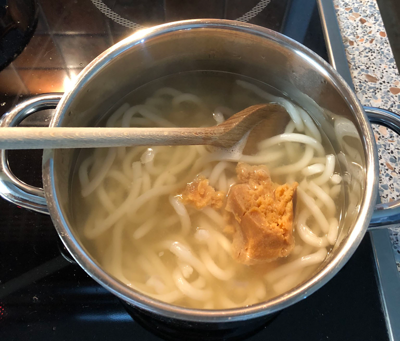 Added udon noodles into dashi and stirring in miso paste